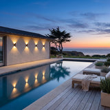 Sunset Wall Light mounted on a pool house wall, reflected in the water at dusk