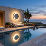 Eclipse Glow Outdoor Light mounted on a pool house wall, reflected in the water at dusk