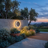 Eclipse Glow Outdoor Light mounted on a garden wall above planting at dusk