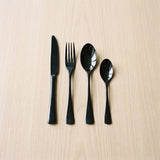 Greece Set — glossy black flatware on a warm wood table