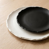 Stone Age Plate Collection — rough-edged matte black and white stone plates on a warm wood table