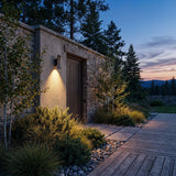 Sunset Wall Light mounted on a garden wall above planting at dusk